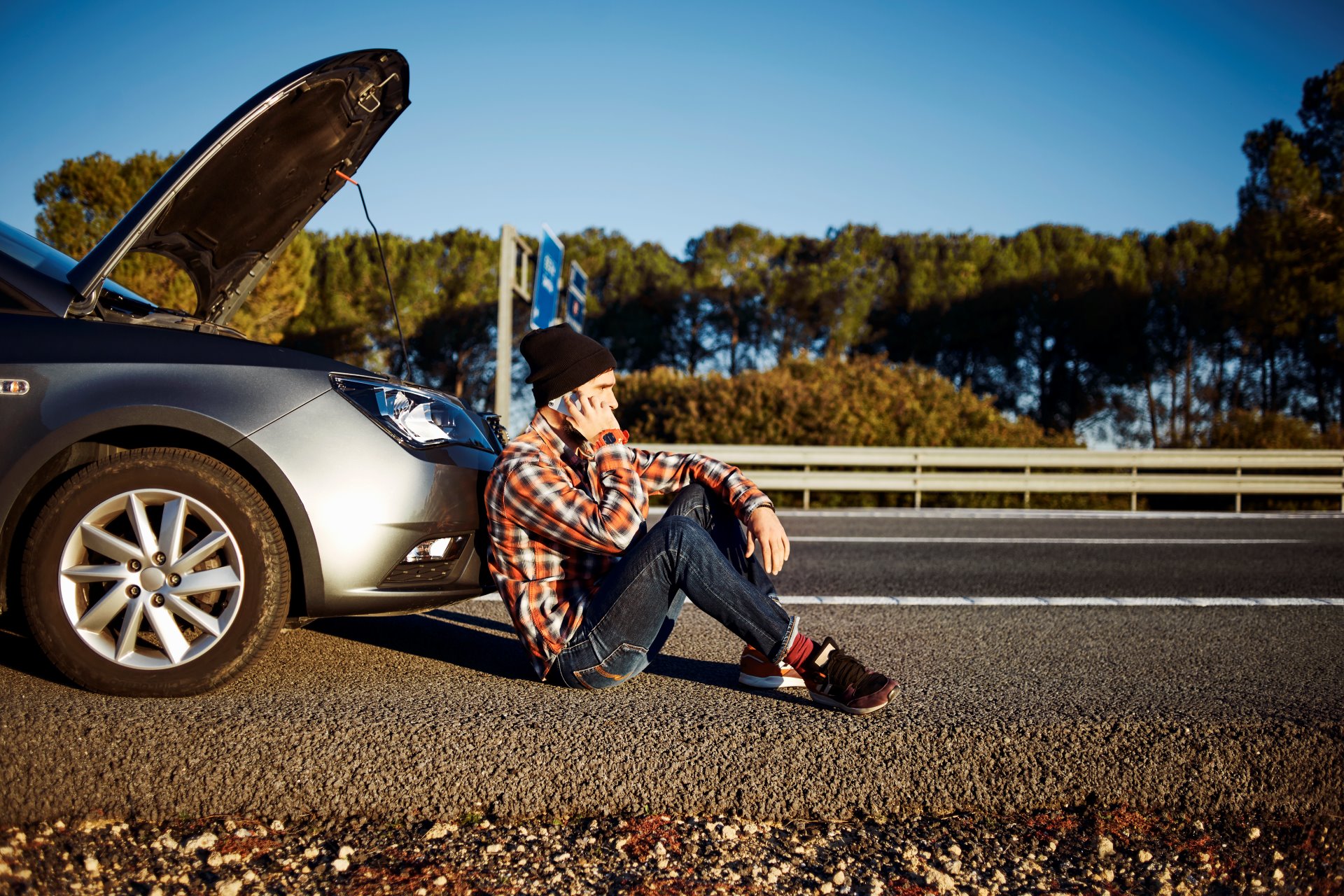 man-talking-phone-leaning-back-front-car-bumper-Car Insurance in Michigan